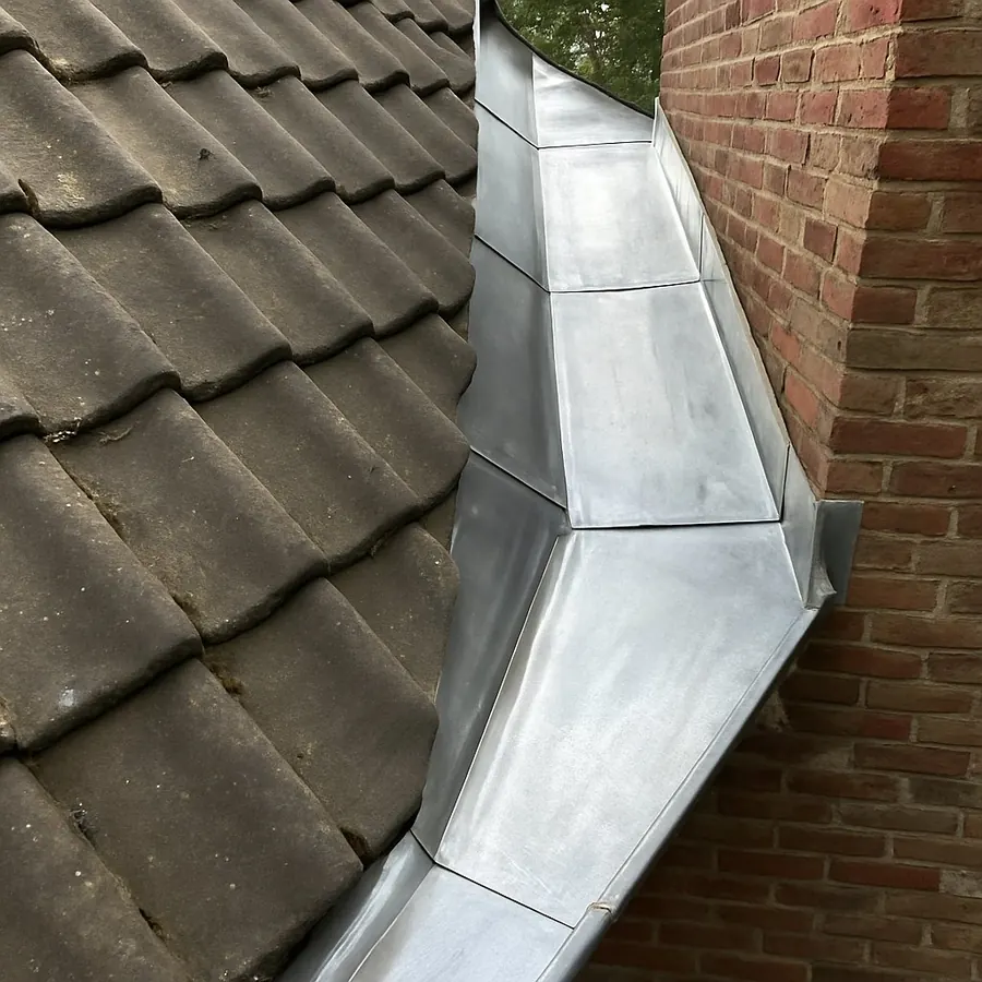 Noue en zinc entre deux pans de toiture en tuiles, contre un mur en briques